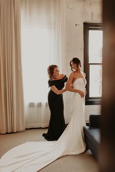 two women standing in front of a window and one is adjusting the bride's dress