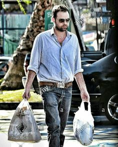 a man walking down the street with two bags in his hand and another bag behind him