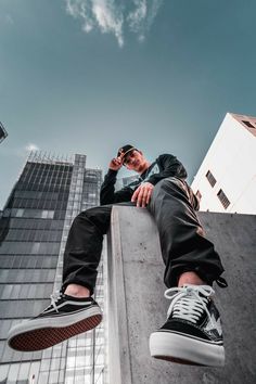 a man sitting on the edge of a building talking on his cell phone while wearing black and white sneakers