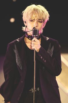 a man with blonde hair holding a microphone in his hand and wearing a black jacket