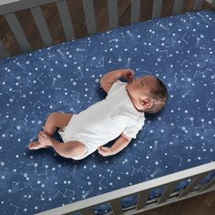 a baby laying on top of a crib next to a blue sheet with stars