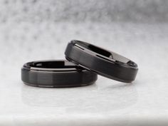 two black wedding bands sitting on top of each other