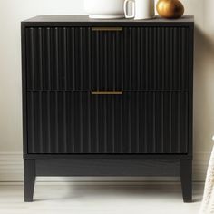 a black cabinet with two drawers and a coffee cup on top, in front of a white wall