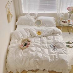 a bed with white comforter and pillows in a small room next to a window