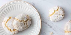 three powdered sugar cookies on a white plate next to another biscuit shaped like a heart