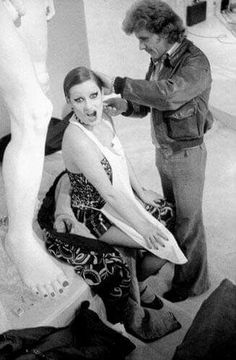 a woman is getting her hair styled by a man in the background, while another person looks on