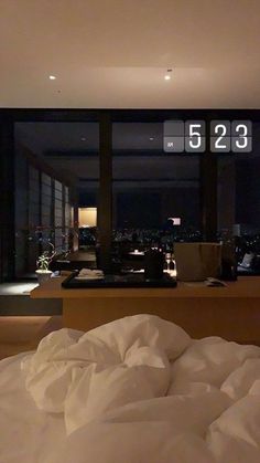 an unmade bed in front of a large window with the city lights lit up