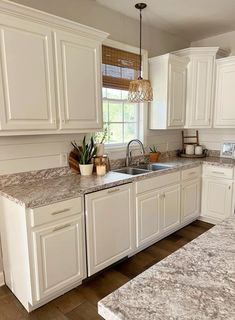 a kitchen with white cabinets and marble counter tops, an island sink and dishwasher