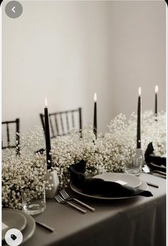 the table is set with black and white plates, silverware, and baby's breath flowers