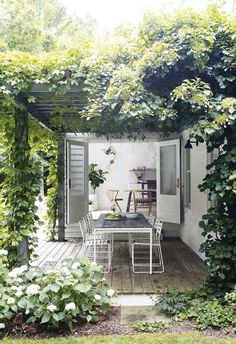 an outdoor dining area with white chairs and table surrounded by greenery on the outside