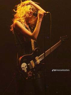 a woman holding a guitar and singing into a microphone