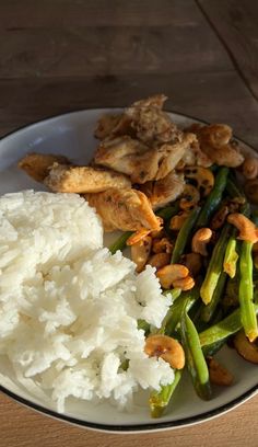 a white plate topped with rice and green beans next to broccoli on top of a wooden table