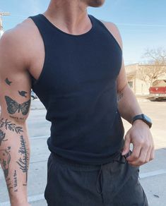 a man with tattoos on his arm and chest standing in the street looking at something