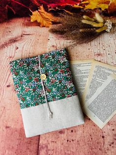 an open book sitting on top of a wooden table next to some leaves and flowers