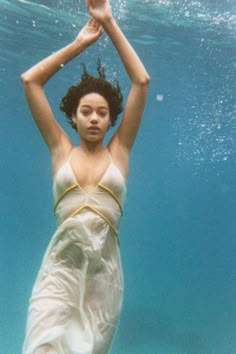 a woman in a white swimsuit under the water with her arms above her head