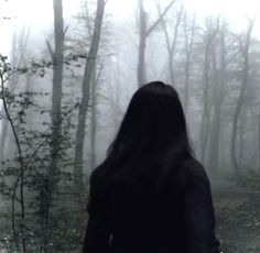 a woman standing in the woods with her back to the camera, looking at trees