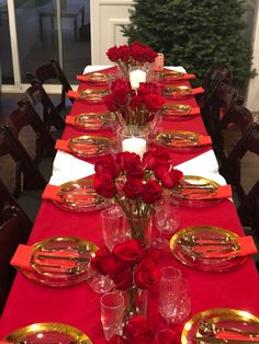 the table is set with red roses and place settings