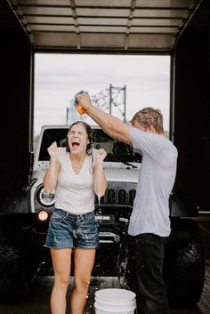 a man and woman standing in front of a white truck spraying water on each other