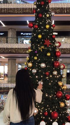 a woman standing next to a christmas tree in a shopping mall with lights on it