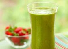 a green smoothie with strawberries in the background