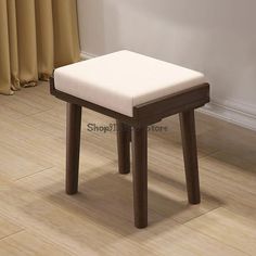 a small wooden stool sitting on top of a hard wood floor next to a window