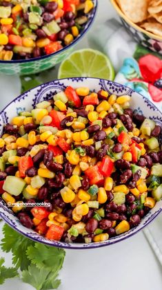 two bowls filled with black beans and corn next to tortilla chips on a table