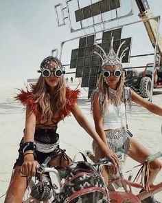 two beautiful women riding bikes on top of a sandy beach