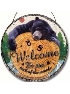 a black bear laying on top of a wooden sign that says welcome to our nature and of the woods