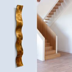 a wooden stair case next to a white wall with a gold metal sculpture on it