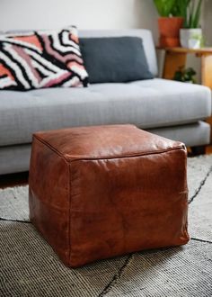 a brown leather ottoman sitting on top of a rug in front of a gray couch