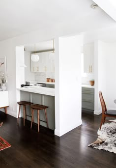 an open kitchen and dining room area with white walls, wood flooring and wooden chairs