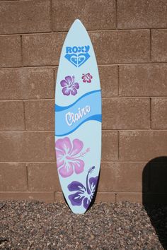 a white surfboard with purple and blue flowers on it next to a brick wall