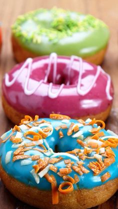 three donuts with different colored frosting and sprinkles sitting on a table