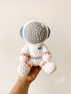 a hand holding a small crocheted white and orange teddy bear with blue eyes