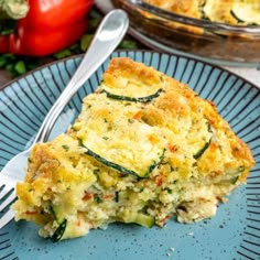 a slice of quiche on a blue plate with a fork and tomatoes in the background