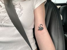 a woman's arm with a black swan tattoo on her left arm, sitting in the back seat of a car