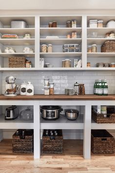 an organized kitchen with white cabinets and wood flooring is pictured in this image, the shelves are full of pots and pans