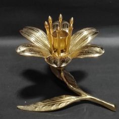 a gold colored flower brooch sitting on top of a black surface with two leaves