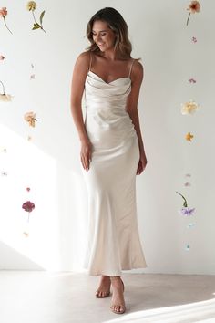 a woman wearing a white dress standing in front of a wall with flowers on it