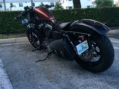 a black motorcycle parked on the street next to some bushes and trees in front of a house