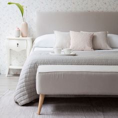 a bed with pillows and blankets on top of it next to a night stand in front of a wallpapered wall