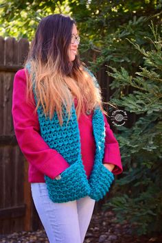 a woman standing in front of a tree wearing a blue and pink knitted vest