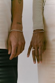 two people holding hands with tattoos on their arms and wristbands, both wearing bracelets