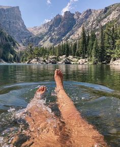 a person laying down in the water with their feet up and mountains in the background