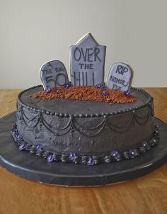 a decorated cake with tombstones and purple flowers on the top is sitting on a wooden table