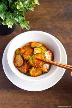 a person holding chopsticks in a bowl of food with sauce and vegetables on the side