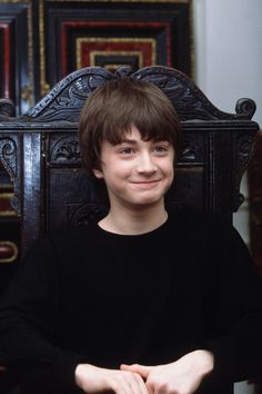 a young boy sitting in a chair with his hands on the table and smiling at the camera