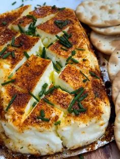 some crackers and cheese are sitting on a wooden table with green garnish