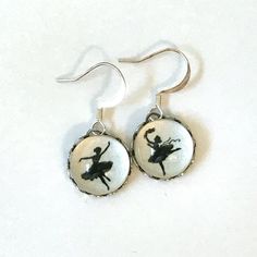 a pair of dangle earrings with an image of a ballerina on it's back