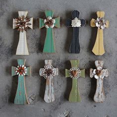 nine wooden crosses are arranged in rows on a gray surface, each with different designs and colors